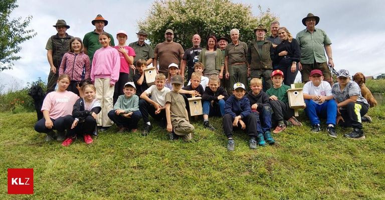 Eine Gruppe von Menschen, Erwachsene und Kinder, posiert für ein Foto auf einem Rasen mit Vogelhäusern vor ihnen.