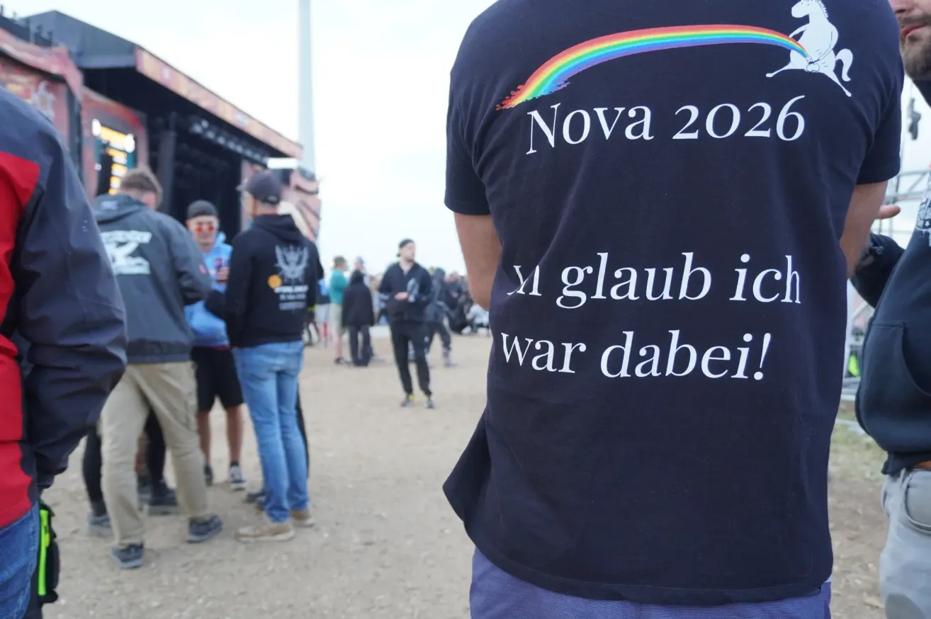 Eine Menschenmenge versammelt sich vor einer Bühne, ein Mensch im blauen T-Shirt sagt 'Ich glaube, ich war dabei!' Die Bühne hat einen Regenbogen und das Wort 'Nova 202' darauf.