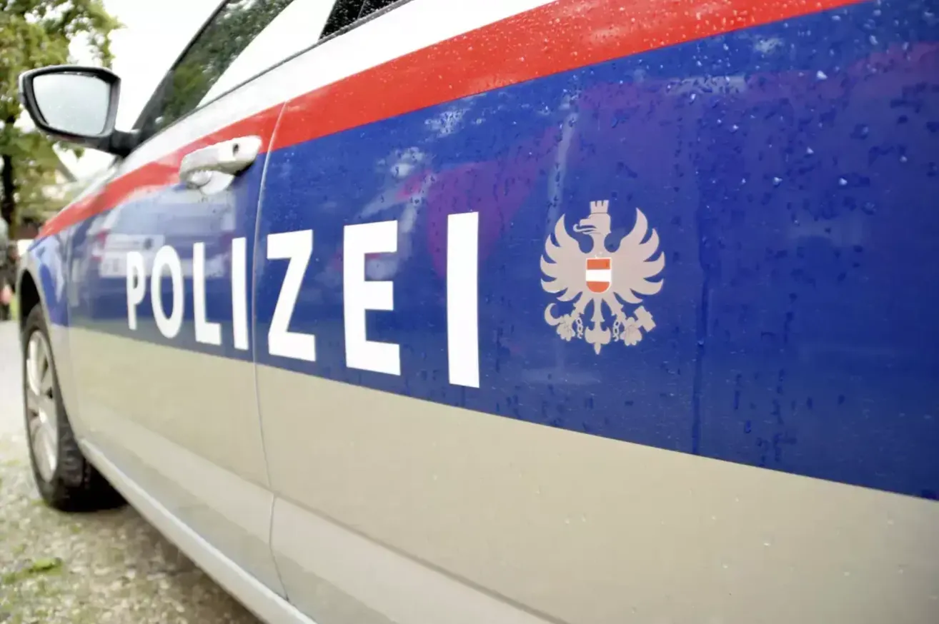 Ein Polizeiauto mit blauen, weißen und roten Streifen. Das Wort 'POLIZEI' ist in Weiß auf der Seite geschrieben. Es gibt ein Logo eines Vogels mit Krone auf der Seite.