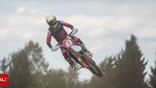 Ein Motorradfahrer in einem roten Rennanzug und Helm, Nummer 8, ist mitten in der Luft auf einem Motocross-Bike. Der Himmel ist bewölkt.