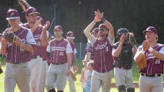 Ein Baseballteam feiert auf dem Feld. Ein junges Mädchen in einem rosa Kleid schaut zu.