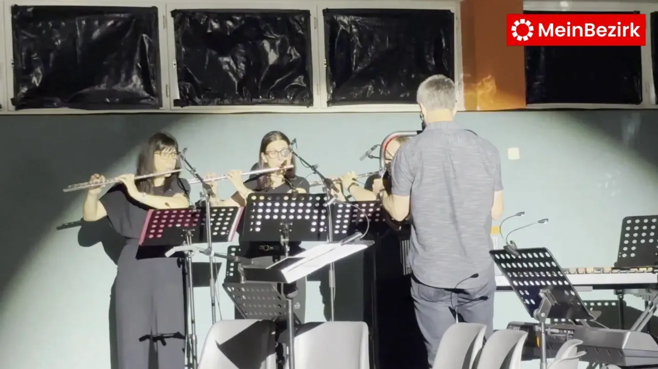 Four women playing flutes with music stands in front of them, a man stands behind them.