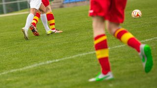 Fußballspieler in roten und weißen Trikots auf einem Rasenfeld, ein Spieler im Fokus mit roten und gelben gestreiften Socken.