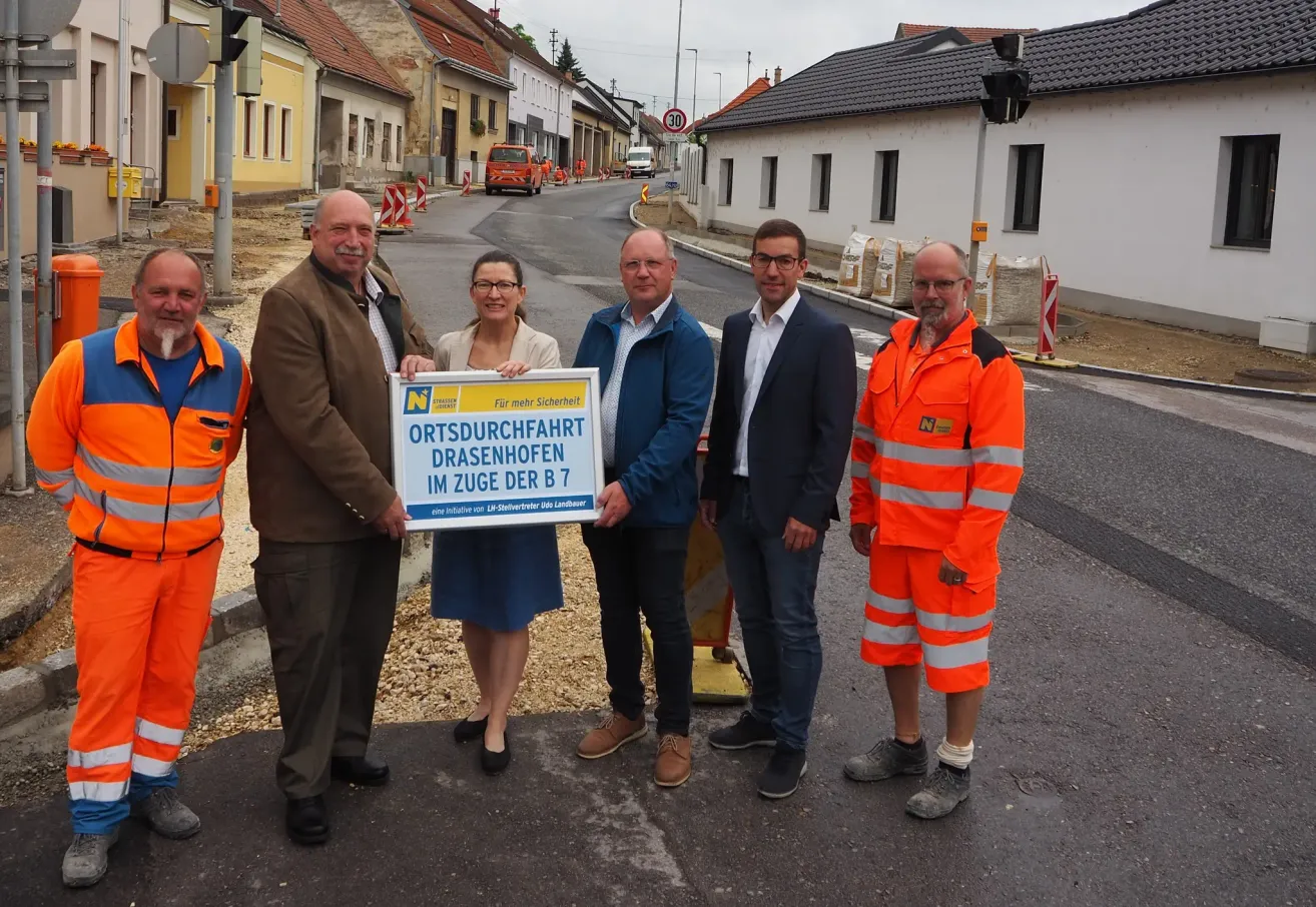 Fünf Personen stehen in einer Gruppe auf einer Straße. Eine Person hält ein Banner mit der Aufschrift Ortsdurchfahrt Drasenhofen im Zuge der B 7.