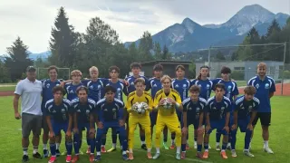 Eine Fußballmannschaft in blauen Uniformen posiert für ein Foto auf einem Feld mit Bergen im Hintergrund.