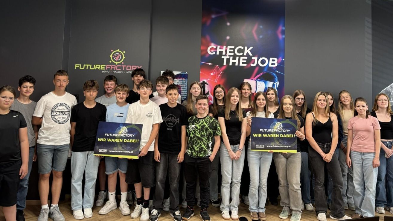 Eine Gruppe junger Menschen posiert für ein Foto vor einem Banner mit den Worten Check the Job. Sie halten Schilder, auf denen Futurefactory Wir waren dabei! steht und tragen Freizeitkleidung. Das Banner hinter ihnen hat ein farbenfrohes Design.