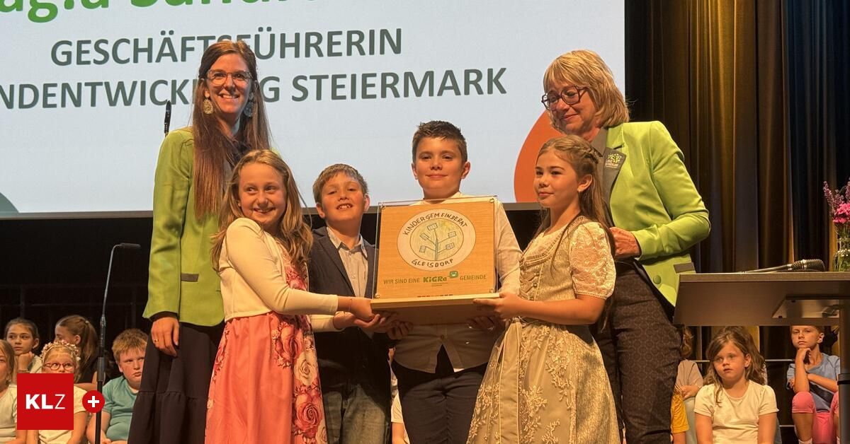 Eine Gruppe von Kindern, die eine Plakette mit einem Baumdesign in der Hand halten, steht vor einer großen Leinwand.