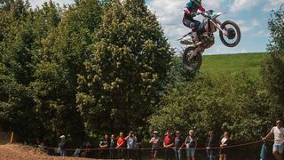 Ein Motocross-Fahrer springt über einen Hügel, umgeben von einer Menge Zuschauer, die das Ereignis verfolgen.