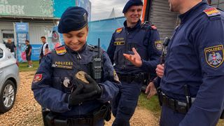 Drei Polizisten in Uniform stehen draußen. Eine Frau hält ein kleines Tier in den Händen. Sie sieht glücklich aus. Ein anderer Polizist sieht sie lächelnd an.