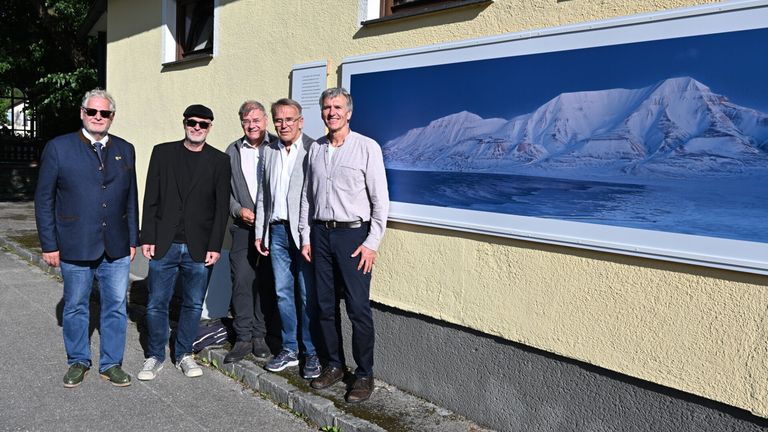 Vier Männer stehen vor einem Gebäude mit einem großen gerahmten Bild von verschneiten Bergen an der Wand.