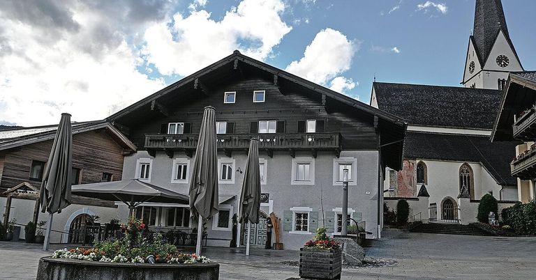 Ein traditionelles Gebäude mit schwarzer Fassade, weißen Fenstern und einem Balkon im zweiten Stock. Vor dem Gebäude stehen drei geschlossene Regenschirme.