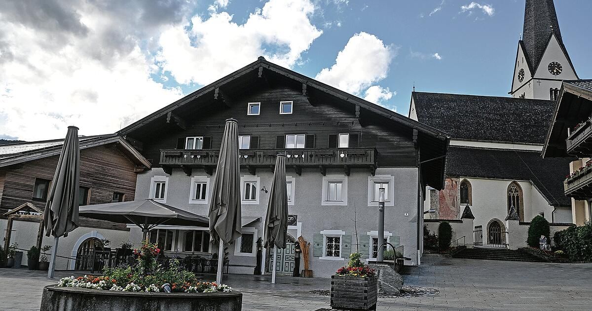 Ein traditionelles Gebäude mit schwarzer Fassade, weißen Fenstern und einem Balkon im zweiten Stock. Vor dem Gebäude stehen drei geschlossene Regenschirme.