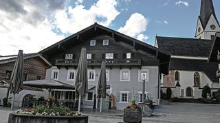 Ein traditionelles Gebäude mit schwarzer Fassade, weißen Fenstern und einem Balkon im zweiten Stock. Vor dem Gebäude stehen drei geschlossene Regenschirme.