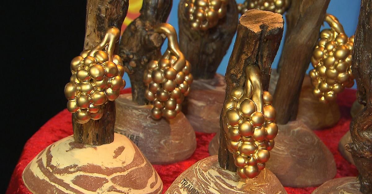 Eine Nahaufnahme mehrerer dekorativer Objekte, die aus Holz gefertigt und mit goldenen Trauben verziert sind. Die Objekte stehen auf einer roten Oberfläche.