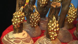 Eine Nahaufnahme mehrerer dekorativer Objekte, die aus Holz gefertigt und mit goldenen Trauben verziert sind. Die Objekte stehen auf einer roten Oberfläche.