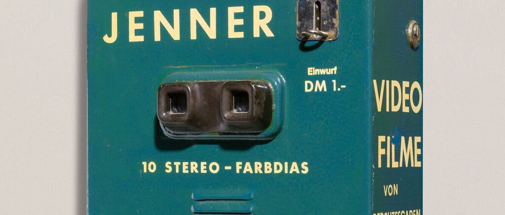 A green box with a metal lock and a stereo viewer on it. It says Jenner, 10 stereo Farbdias, and Einwurf DM 1.-. Video Filme von.