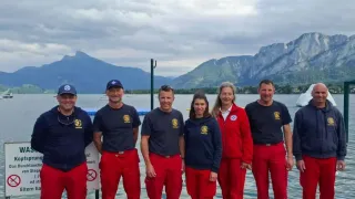 Eine Gruppe von Menschen in roten Uniformen posiert für ein Foto auf einem Steg mit Bergen im Hintergrund.