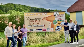 A group of people are posing for a photo in front of a sign advertising the Kirchbach Zerlach Wirtschaftsmesse on June 20 and 21, 2026.