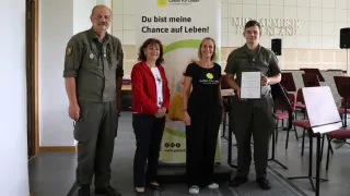 Vier Personen stehen hinter einem Banner mit der Aufschrift Du bist meine Chance auf Leben. Ein Mann auf der rechten Seite hält eine Urkunde.
