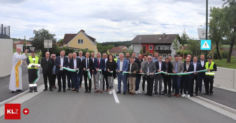 Eine Gruppe formell gekleideter Männer und Frauen steht mit grünen Bändern auf einer Straße, wahrscheinlich zur Feier eines Bandabschneidens.