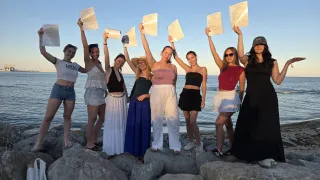 Eine Gruppe von Frauen, die Urkunden halten, steht auf Felsen am Meer und posiert lächelnd für ein Foto.