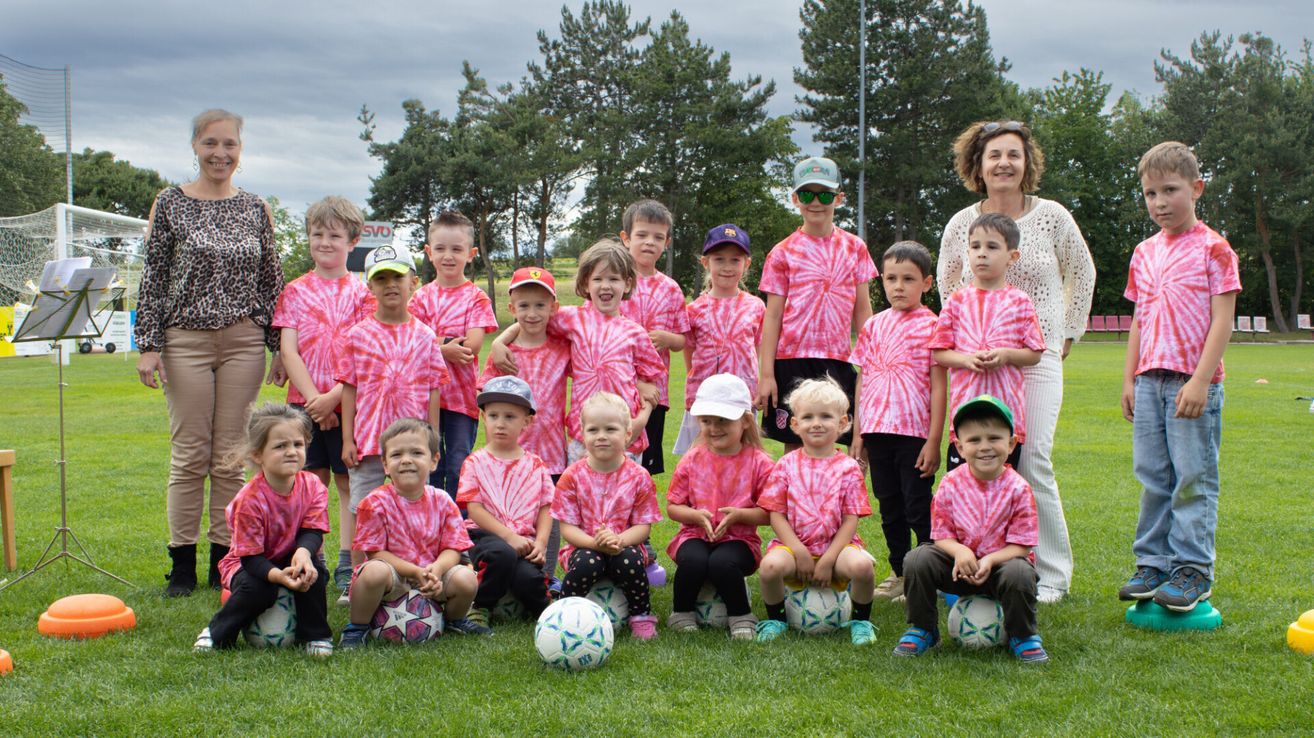Eine Gruppe junger Kinder in rosafarbenen T-Shirts posiert für ein Foto auf einem Rasenfeld mit Fußballbällen.