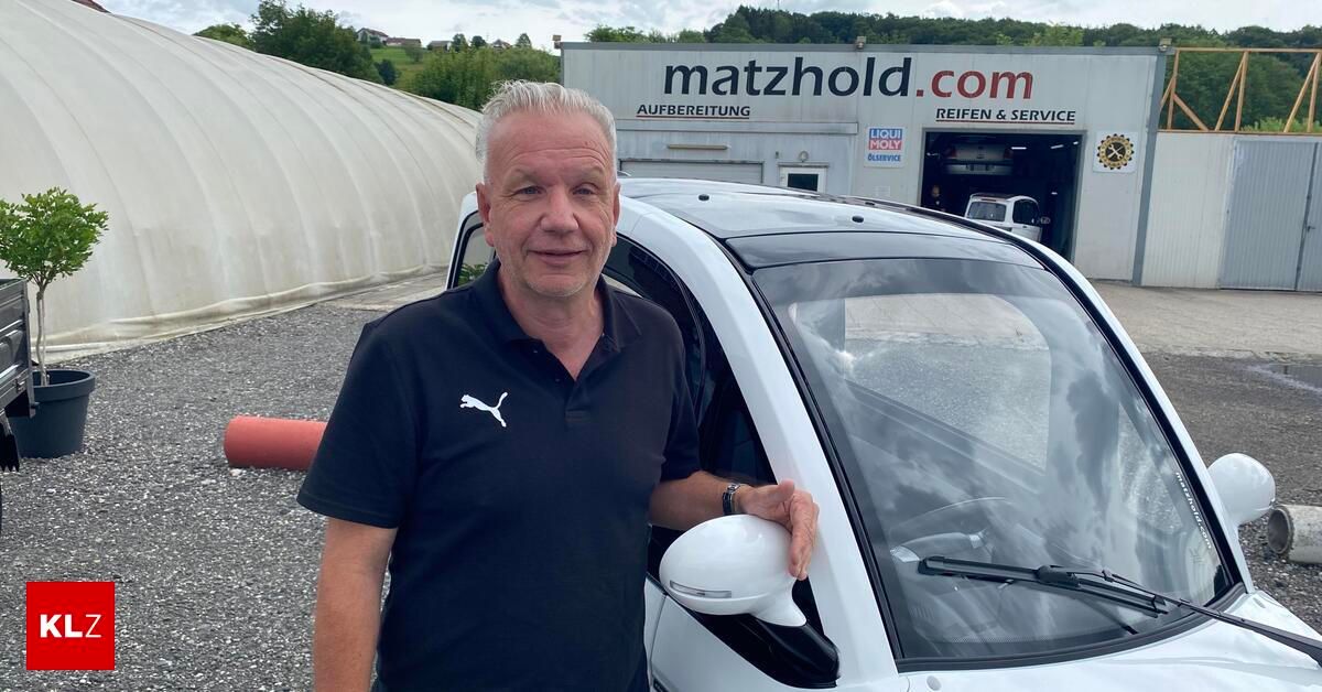 Ein Mann steht neben einem weißen Auto und hält dessen Türspiegel. Hinter ihm befindet sich ein Gebäude mit der Aufschrift 'matzhold.com'.