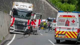 Rettungskräfte kümmern sich um einen verunfallten Lkw auf einer Straße mit einer Steinmauer am Rand.