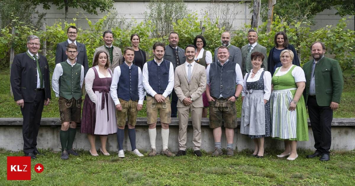 Eine Gruppe von Menschen in traditioneller Kleidung posiert für ein Bild auf einem Rasen, mit einer Betonmauer und Grünpflanzen dahinter.