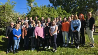 Eine Gruppe von Erwachsenen und Teenagern posiert für ein Foto auf einer Rasenfläche mit Bäumen im Hintergrund. Sie sind alle lässig gekleidet und scheinen für die Kamera zu lächeln.