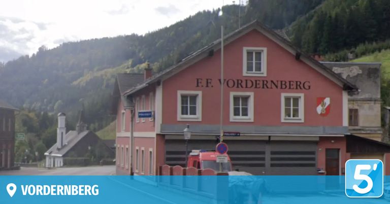 Ein rotes Gebäude mit weißen Fenstern, namens F.F. Vordernberg, hat einen roten Krankenwagen davor geparkt. Das Gebäude befindet sich vor einem Berg.