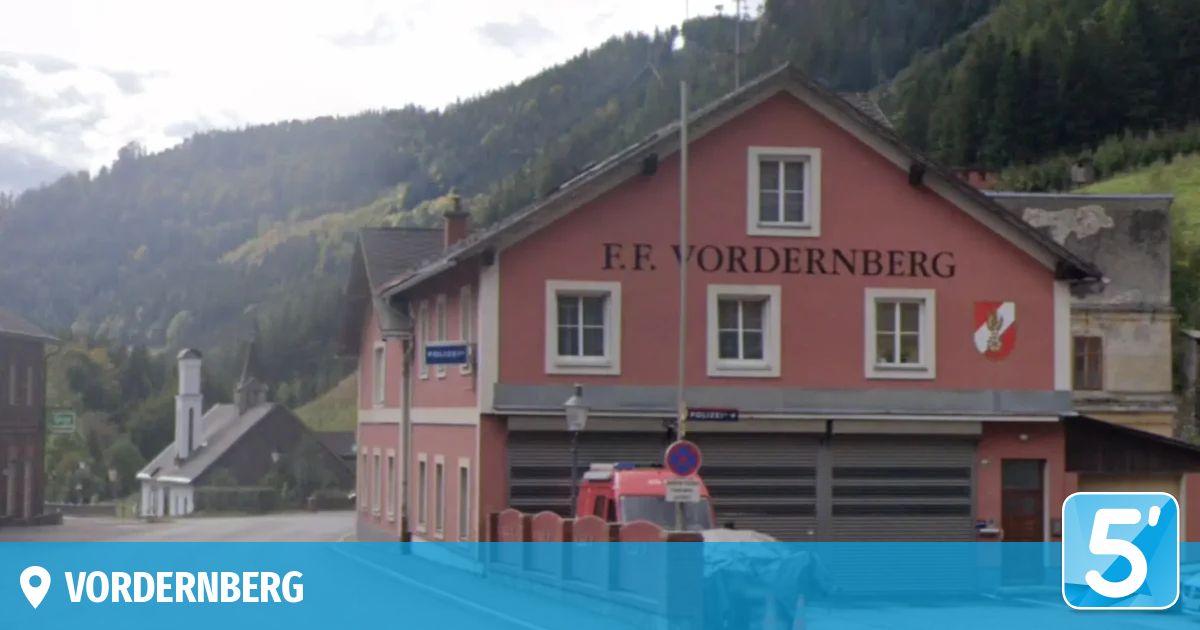 Ein rotes Gebäude mit weißen Fenstern, namens F.F. Vordernberg, hat einen roten Krankenwagen davor geparkt. Das Gebäude befindet sich vor einem Berg.