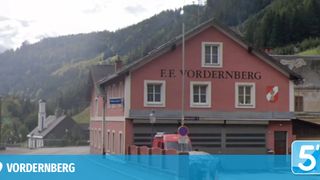 Ein rotes Gebäude mit weißen Fenstern, namens F.F. Vordernberg, hat einen roten Krankenwagen davor geparkt. Das Gebäude befindet sich vor einem Berg.