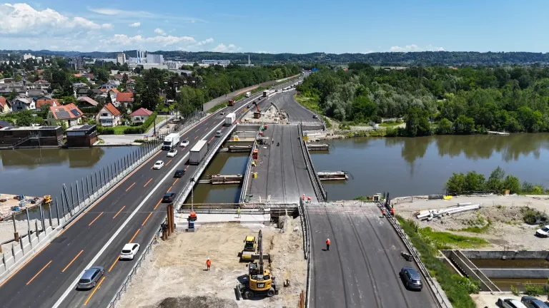 Eine Luftaufnahme einer Baustelle mit einer Brücke über einem Gewässer, Arbeitern, Maschinen und Fahrzeugen auf der Baustelle.