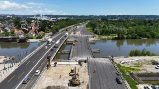 Eine Luftaufnahme einer Baustelle mit einer Brücke über einem Gewässer, Arbeitern, Maschinen und Fahrzeugen auf der Baustelle.