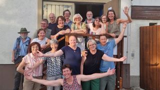 Eine Gruppe von Menschen, hauptsächlich Frauen, lächelt und posiert für ein Foto auf einer Holzveranda mit einer Tür dahinter.