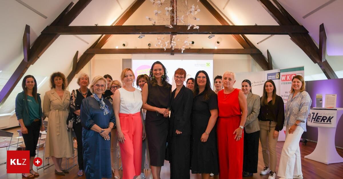 Eine Gruppe von Frauen in formeller Kleidung posiert für ein Foto in einem Raum mit Holzbalken, einer Kristallleuchte und einer Projektionsleinwand.