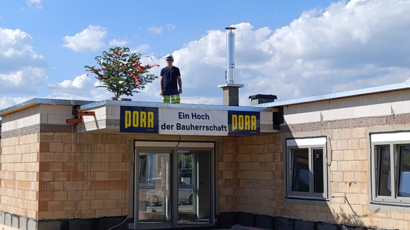 A man stands on a rooftop of a building. The sign reads 'DORR'. He wears a hat and holds a tool.