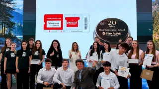 Gruppenfoto von Personen, einige halten Urkunden in der Hand, vor einer großen Leinwand, auf der Bank Austria und Cineplexx Werbung zu sehen ist. Die Leinwand zeigt ein Ticket und einen Next Generation Award.