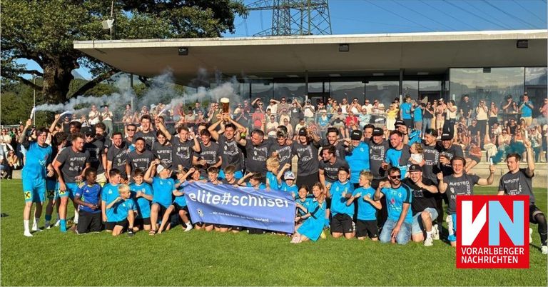 Eine Gruppe von Menschen in blauen Trikots posiert für ein Foto in einem Stadion mit Rauch und einem Banner, das 'elite#schuser' liest.
