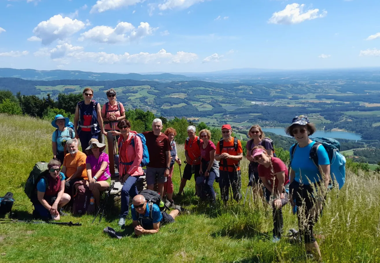 Eine Gruppe von Wanderern, die Mützen und Brillen tragen, posiert auf einem Berg mit Blick auf das Tal. Einige sitzen auf einem Stein, während andere auf dem Gras stehen.