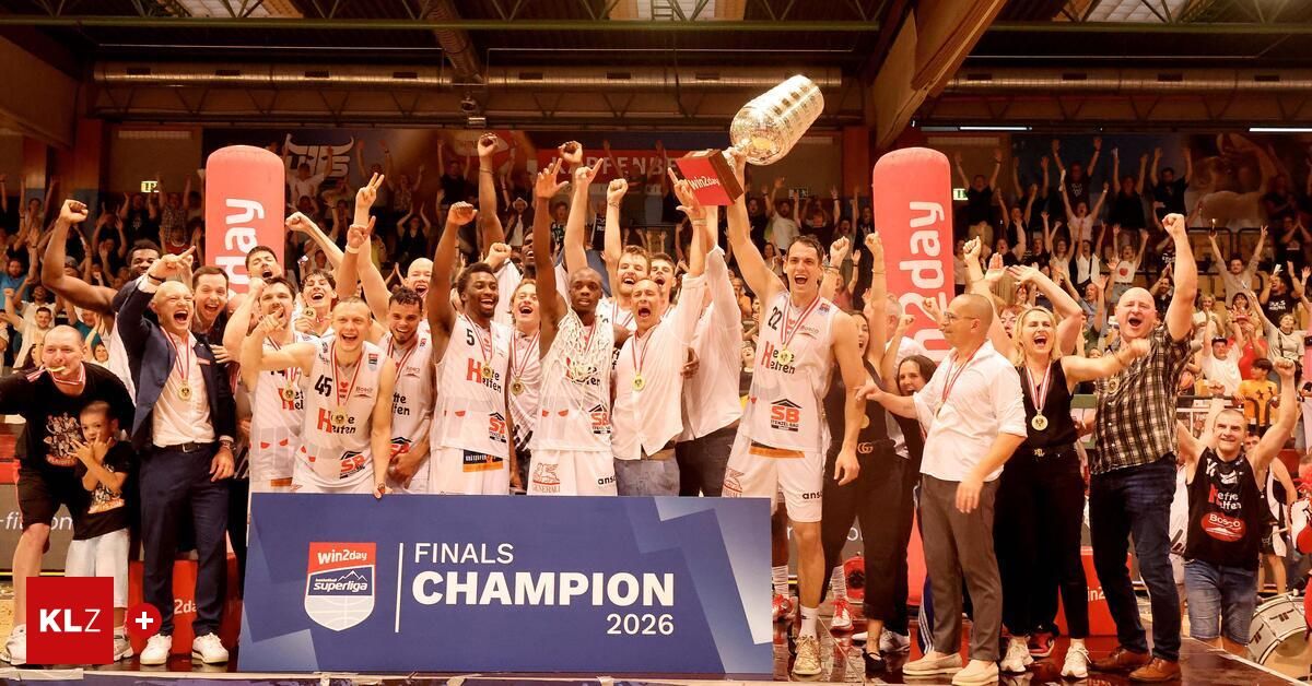Basketball players celebrate with a trophy, wearing white jerseys and medals, in front of a cheering crowd at a sports event in 2016.