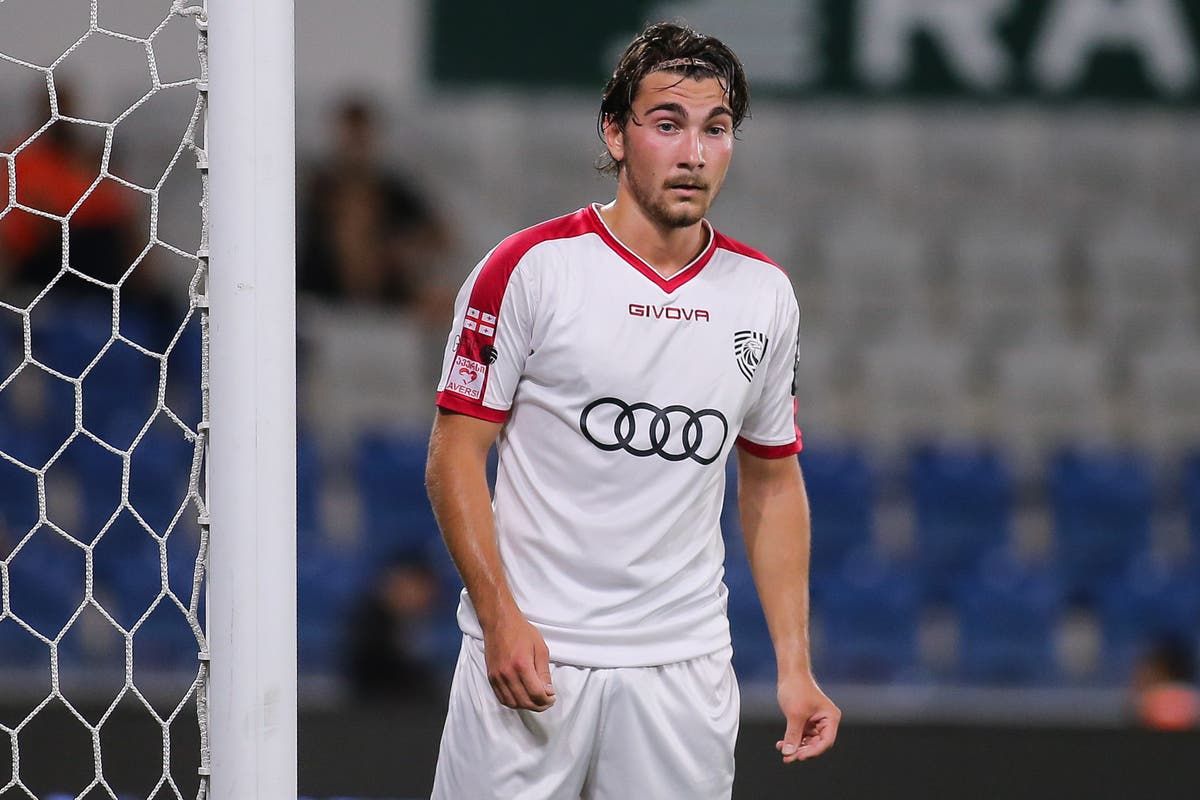Ein Fußballspieler in einem weißen und roten Trikot mit Audi-Logo steht neben einem Torpfosten.