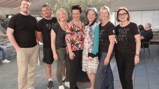 Eine Gruppe von sechs Erwachsenen, vier Frauen und zwei Männer, posiert für ein Foto in einem Flur, wobei zwei Frauen eine Brille tragen.