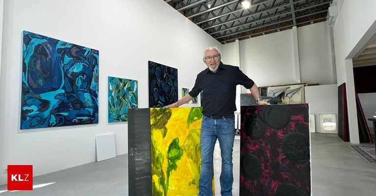 Ein älterer Mann steht in einer Kunstgalerie mit mehreren abstrakten Gemälden hinter ihm, eines davon ist gelb und grün.