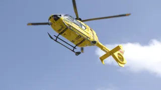 A yellow helicopter with DAMTC and OE-XEQ written on it, flying in the sky with a cloudy background.