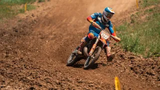 Ein Motocross-Fahrer auf einer staubigen Piste, mit Helm, Handschuhen und Stiefeln. Der Fahrer hat die Nummer 235 auf seinem Motorrad.