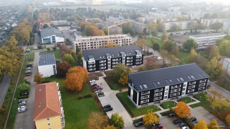 Ein Luftbild einer Wohngegend mit mehreren Mehrfamilienhäusern, einer Baustelle und einem Parkplatz. Bäume und Gras sind in der Gegend verstreut.