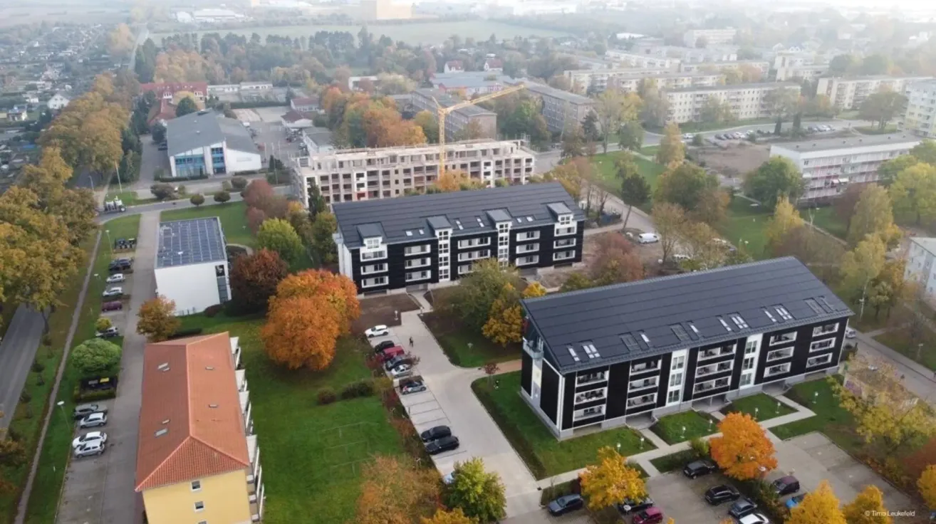 Ein Luftbild einer Wohngegend mit mehreren Mehrfamilienhäusern, einer Baustelle und einem Parkplatz. Bäume und Gras sind in der Gegend verstreut.