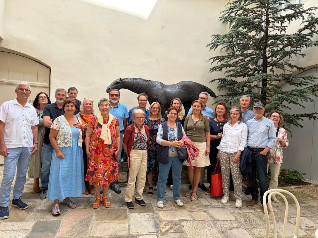 Eine Gruppe von Menschen posiert für ein Foto vor einer Pferdestatue. Sie stehen alle zusammen und lächeln.